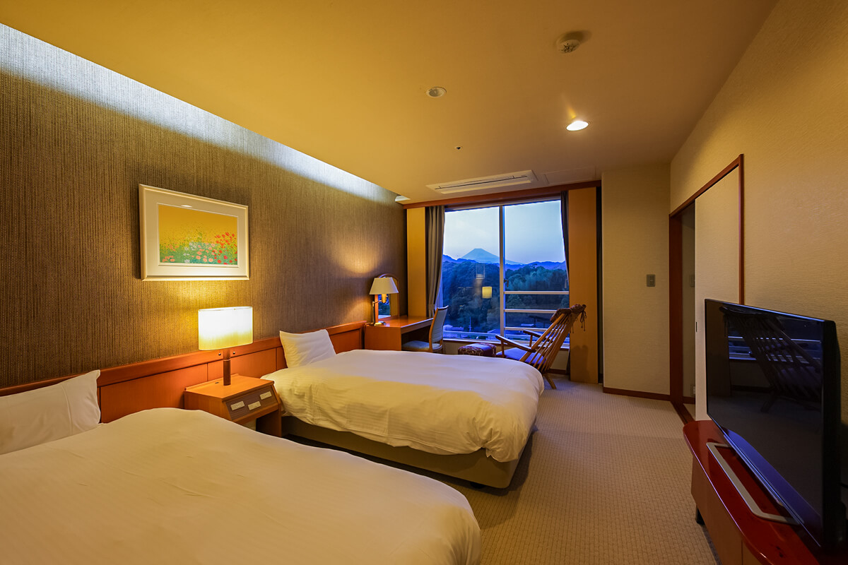 ツインルームのベッドと窓から見える夕方の山々と富士山